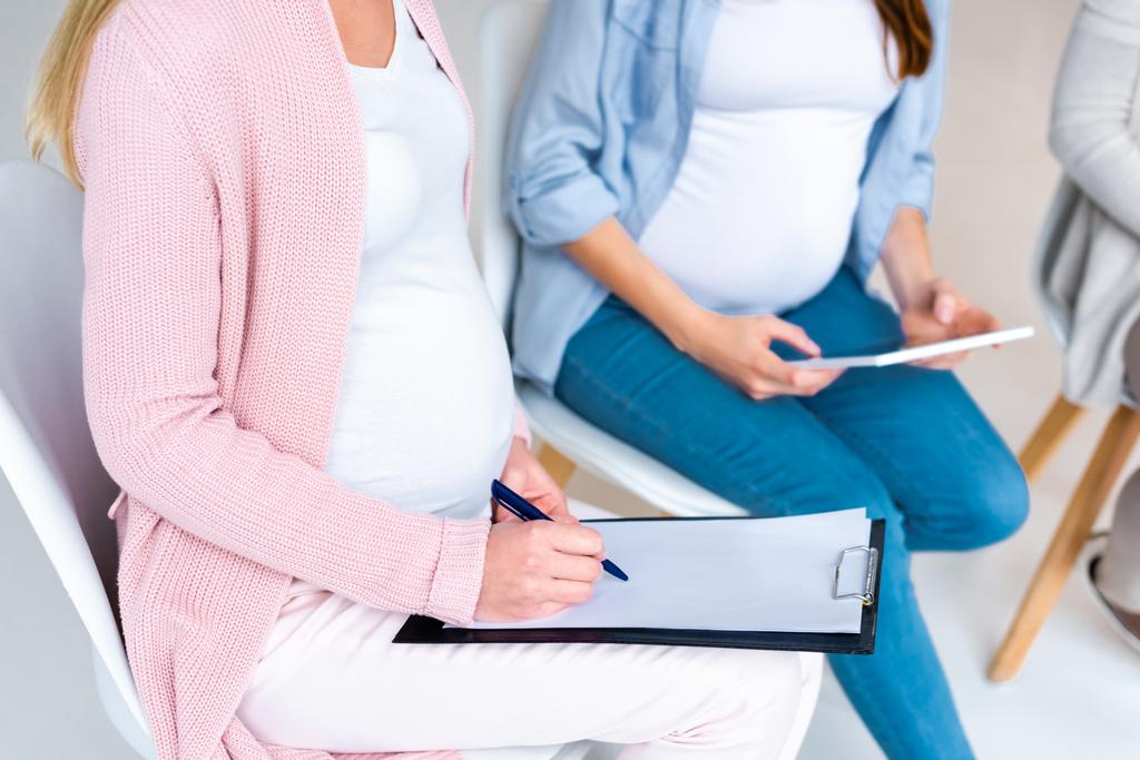 フォームに記入し、グレーに分離された出生前のクラスでデジタル タブレットを使用して妊娠中の女性のトリミング ビュー - 写真・画像