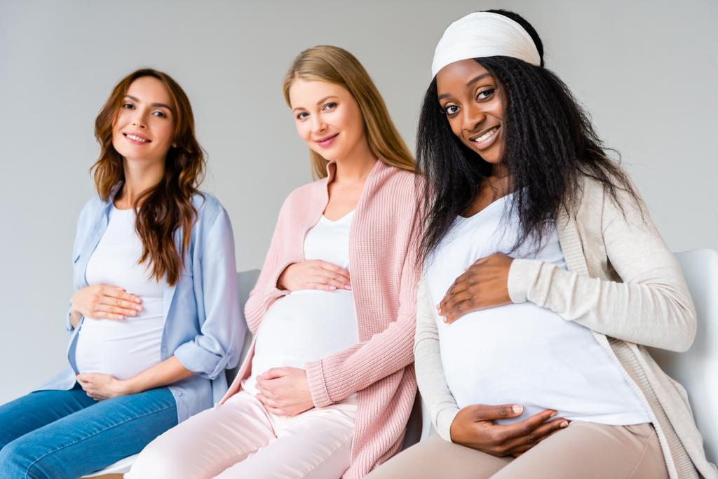 mujeres embarazadas multiétnicas tocando vientres durante la clase prenatal aisladas en gris
 - Foto, Imagen