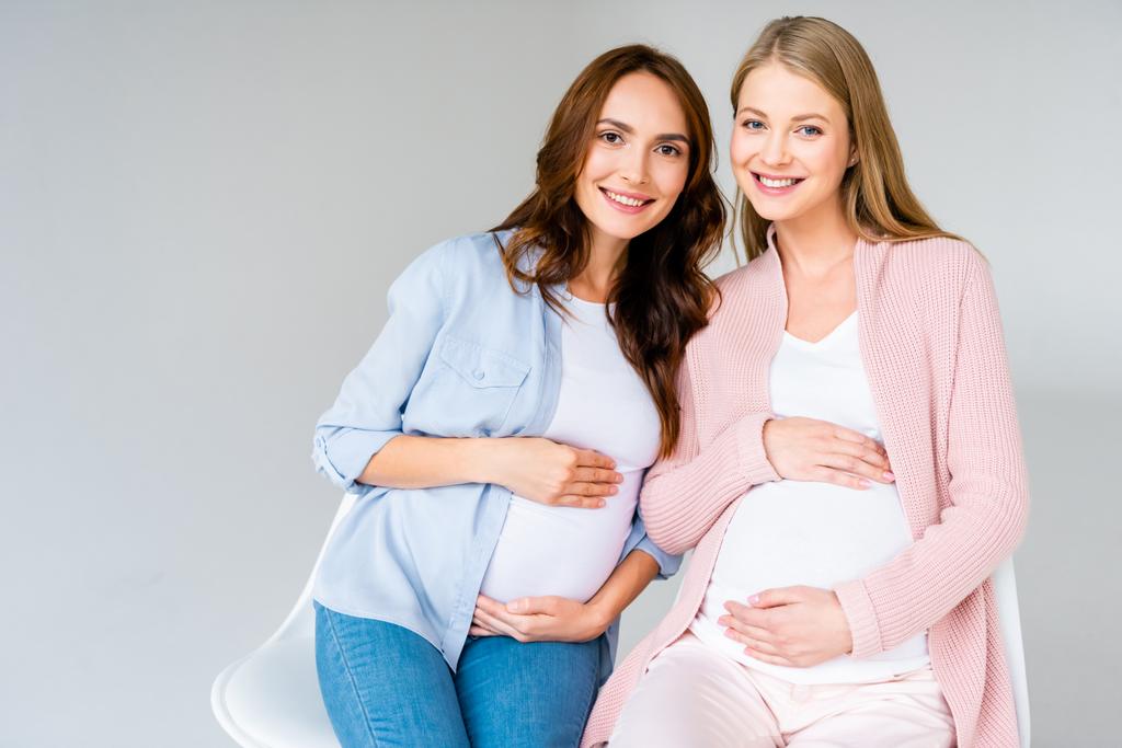 Schwangere lächelnde Frauen sitzen isoliert auf Stühlen in grau - Foto, Bild