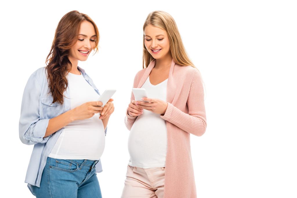 hermosas mujeres embarazadas sonrientes mensajes de texto en teléfonos inteligentes aislados en blanco
 - Foto, imagen