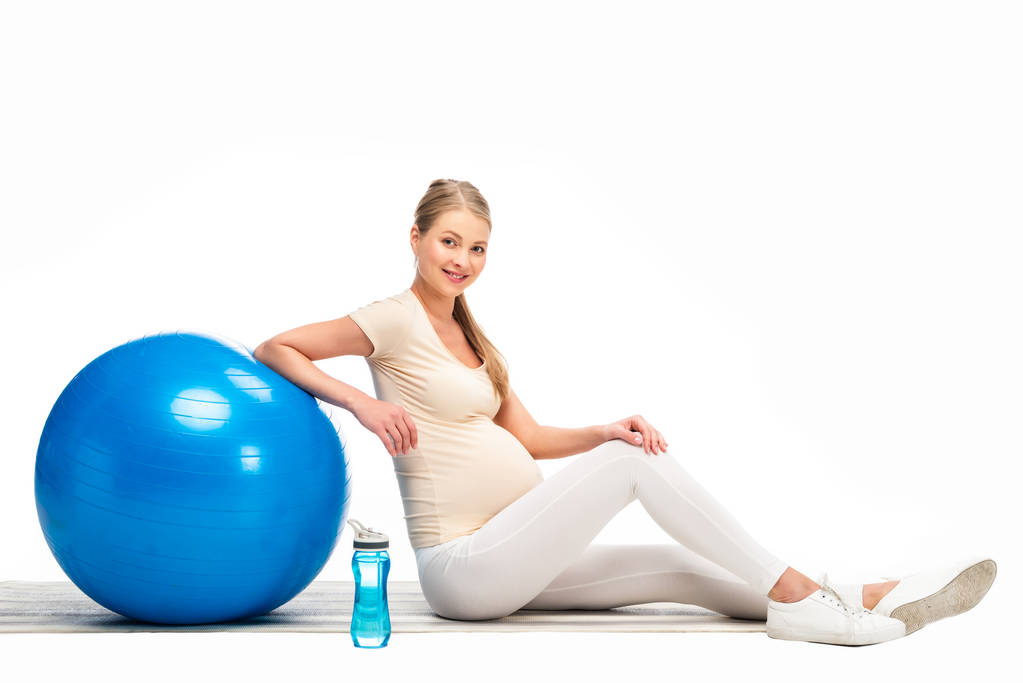 Blonde těhotná žena sedící na podlaze s modrou fitness míč izolované na bílém - Fotografie, Obrázek