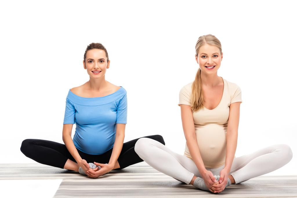 дві вагітні жінки сидять на підлозі і тримають руки на ногах ізольовані на білому
 - Фото, зображення