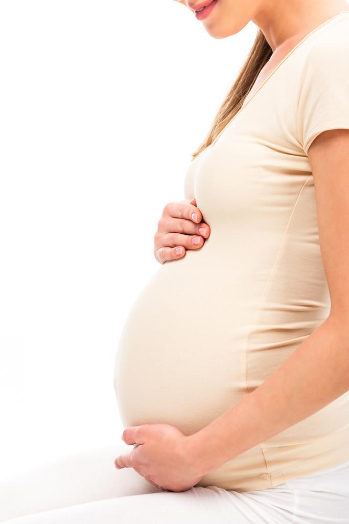 obcięty widok kobiety w ciąży, trzymając ręce na brzuch na białym tle - Zdjęcie, obraz
