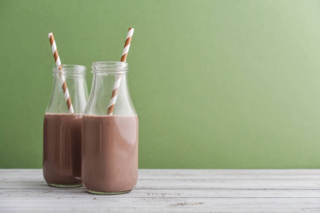 Twee flessen chocolade melk met het drinken van rietjes op groene achtergrond - Foto, afbeelding