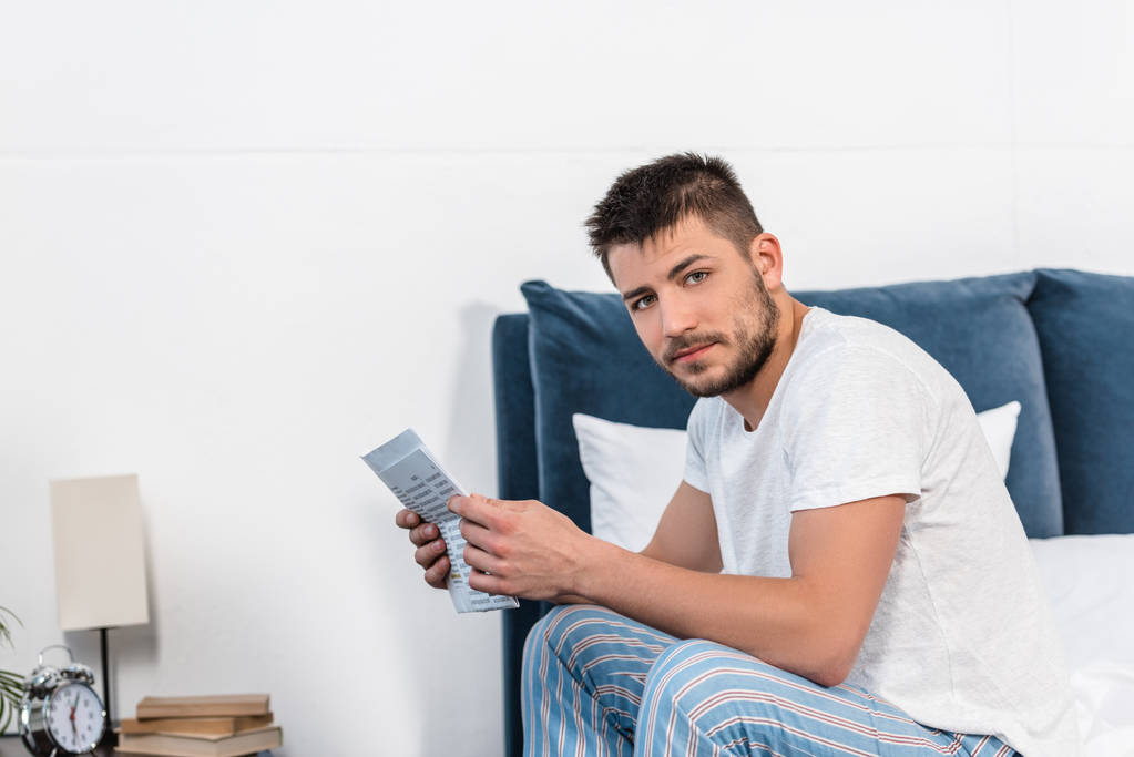 handsome man holding newspaper in bed in morning at home, looking at camera - Photo, Image