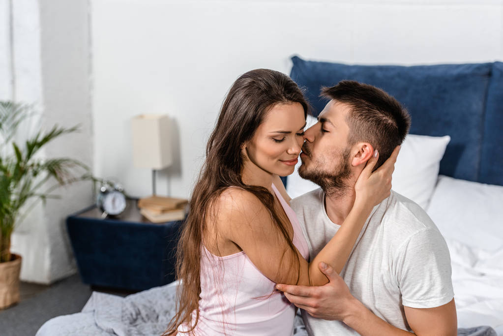 Freund im Pyjama umarmt und küsst Freundin auf Bett im Schlafzimmer - Foto, Bild