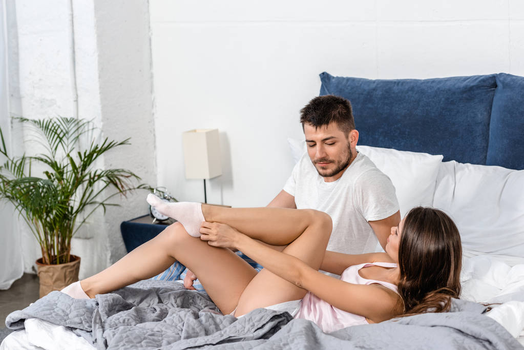 fidanzata sdraiata sul letto, indossando calzini e guardando e fidanzato in pigiama in camera da letto
 - Foto, immagini