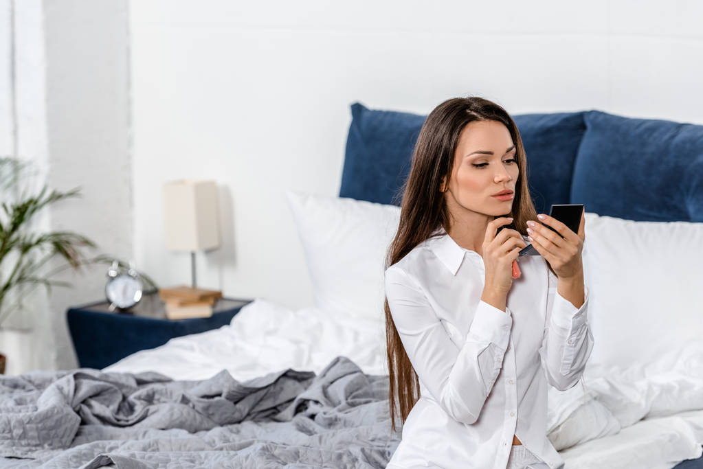 красива жінка сидить на ліжку і дивиться на дзеркало вранці в спальні
 - Фото, зображення