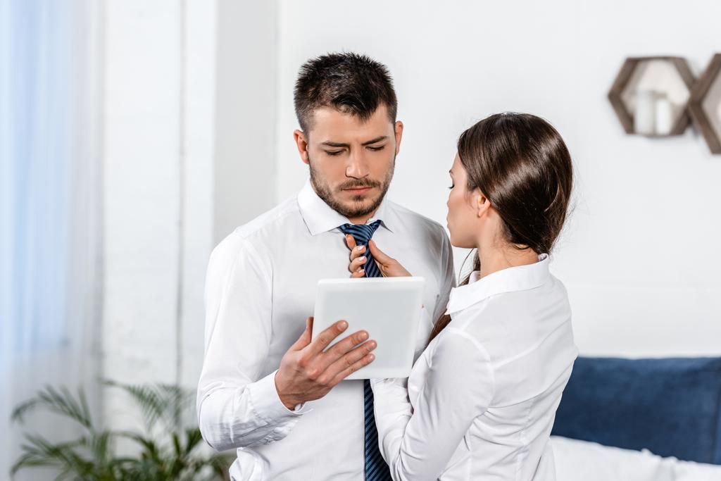namorada amarrando gravata namorado enquanto ele usa tablet de manhã em casa, conceito de papel social
 - Foto, Imagem