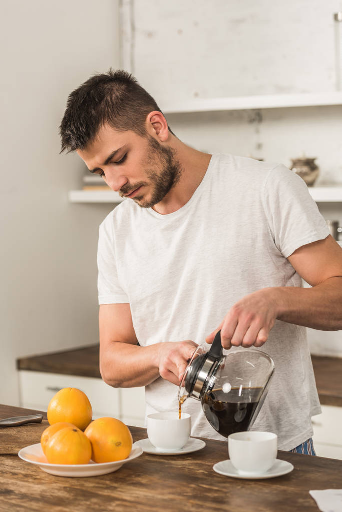 komea mies kaatamalla kahvia kuppiin aamulla keittiössä
 - Valokuva, kuva