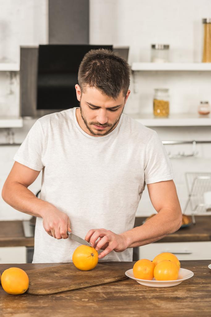 pohledný muž řezání pomeranče v ráno v kuchyni - Fotografie, Obrázek
