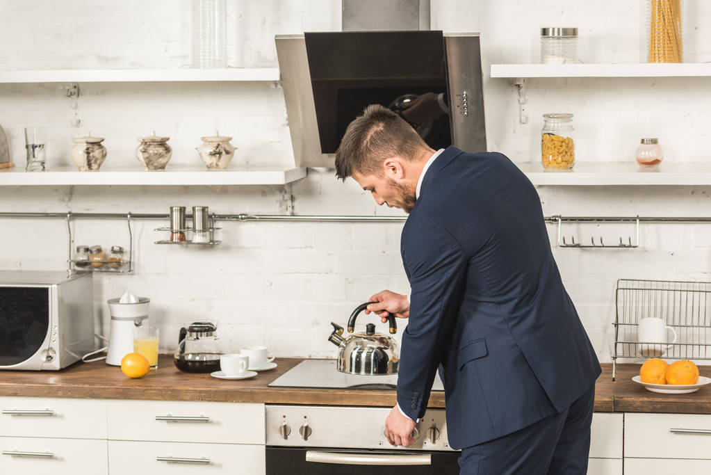 Çaydanlık ocakta sabah mutfağa koyarak takım elbiseli yakışıklı adam - Fotoğraf, Görsel