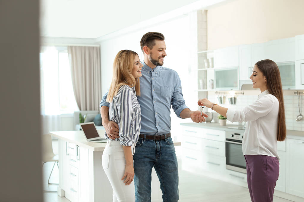 Agente imobiliário feminino dando chave de casa para casal dentro de casa
 - Foto, Imagem