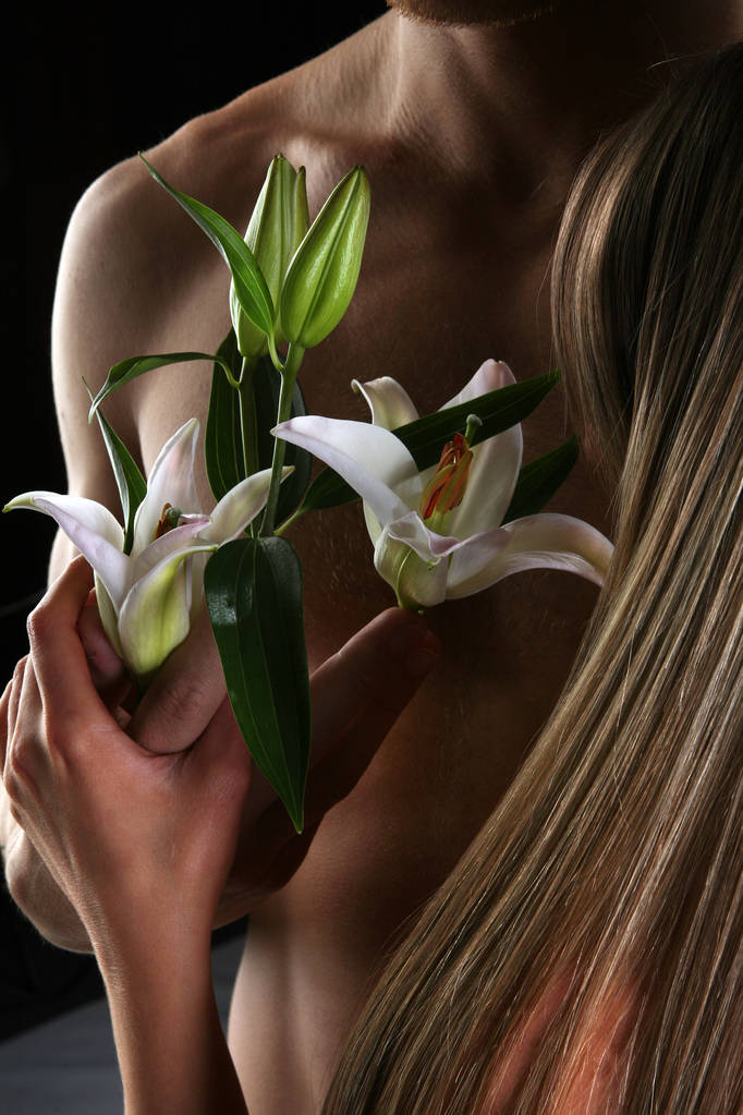 крупным планом белой лилии в руках на фоне обнаженного туловища на темном фоне студии - Фото, изображение