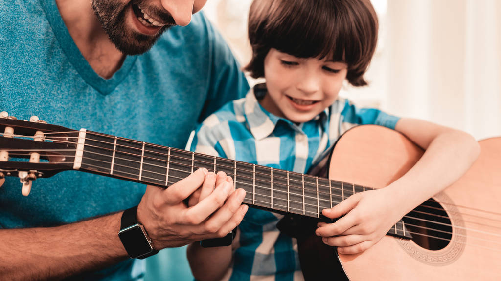 若い髭父の息子とギターで演奏します。幸せな家族の概念。自宅の音楽家。シャツの少年。モダンな趣味概念。音楽と歌の概念。笑みを浮かべて男. - 写真・画像