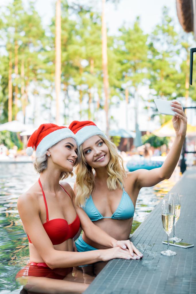 amici sorridenti in cappelli Babbo Natale prendere selfie su smartphone in piscina, concetto di nuovo anno
 - Foto, immagini