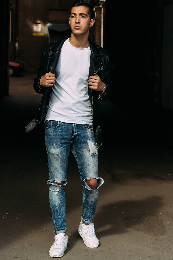 jeune, beau mec dans un T-shirt blanc, noir, veste en cuir et bleu, jeans déchiré est dans la rue, modèle, promenade en ville, en direct style.in baskets blanches
 - Photo, image