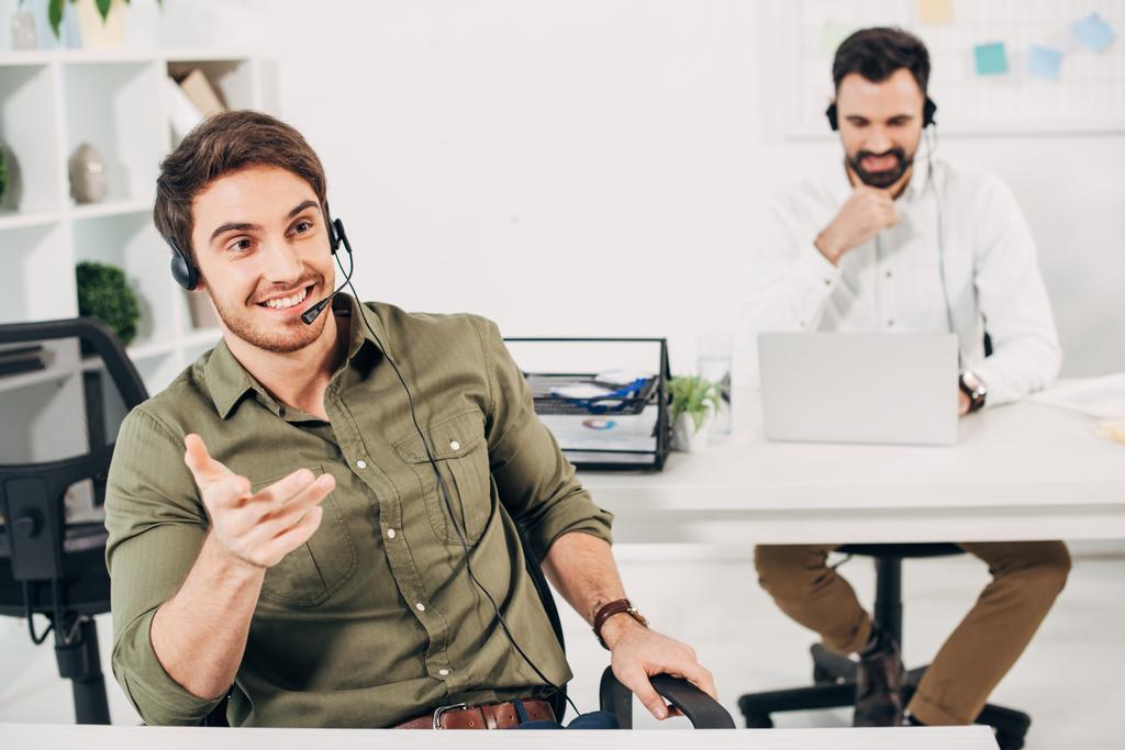 komea puhelinkeskuksen operaattori, jolla on kuulokkeet hymyilevät ja puhuvat toimistossa
 - Valokuva, kuva
