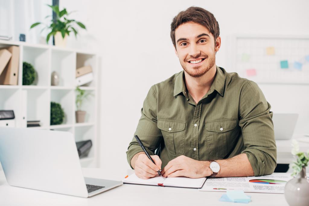 Giovane uomo d'affari sorridente e in possesso di penna in ufficio moderno
  - Foto, immagini