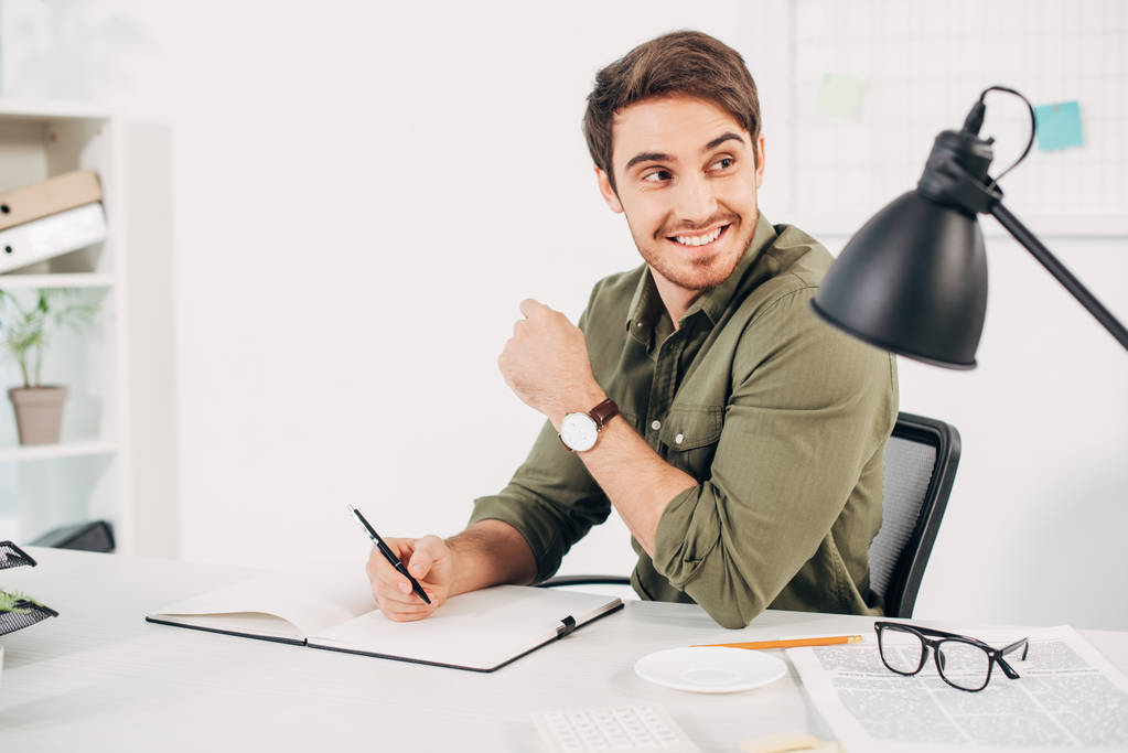 fröhlicher Geschäftsmann lächelt mit Stift in der Hand im Büro  - Foto, Bild