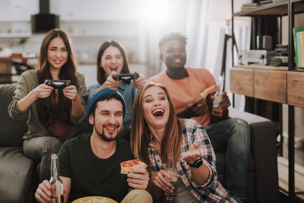Iloiset nuoret pelaavat videopelejä nauttien juomista ja ruoasta
 - Valokuva, kuva