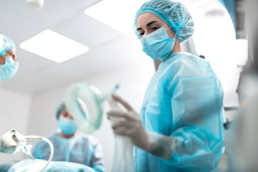 Медицинский работник смотрит на кислородную маску, стоя в операционной
 - Фото, изображение