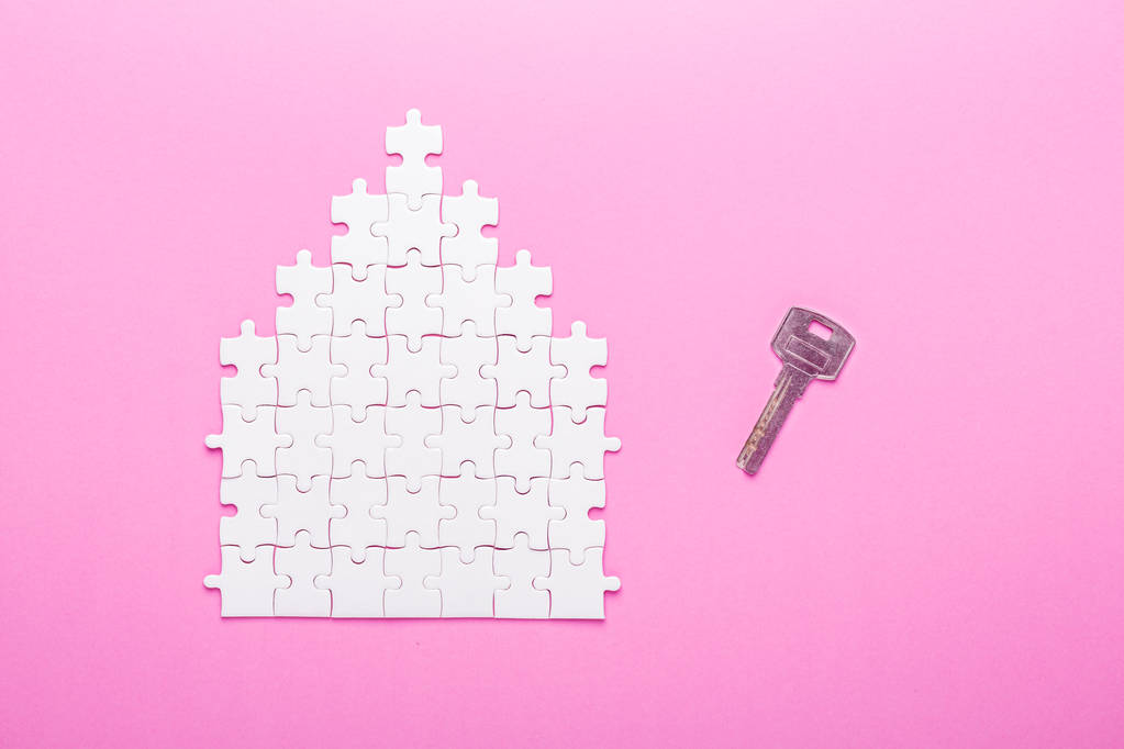 Un puzzle bianco. Forma della casa puzzle e chiave. Il concetto di affitto, ipoteca. Sfondo rosa. Vista dall'alto
 - Foto, immagini