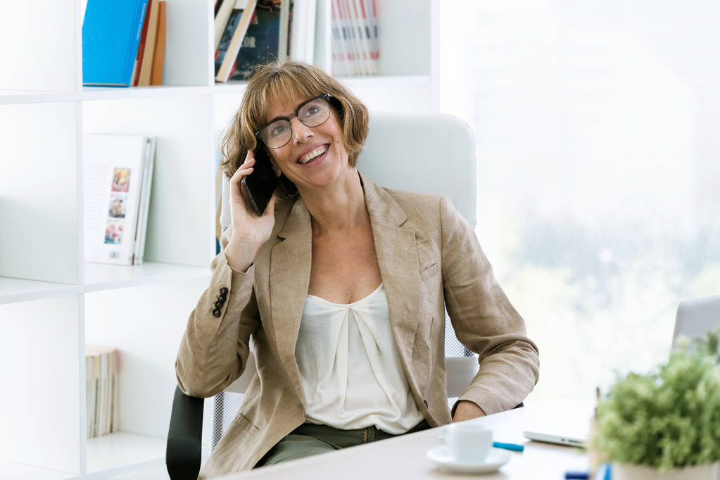 Aufnahme der schönen, glücklichen Geschäftsfrau, die im Büro mit ihrem Handy spricht. - Foto, Bild