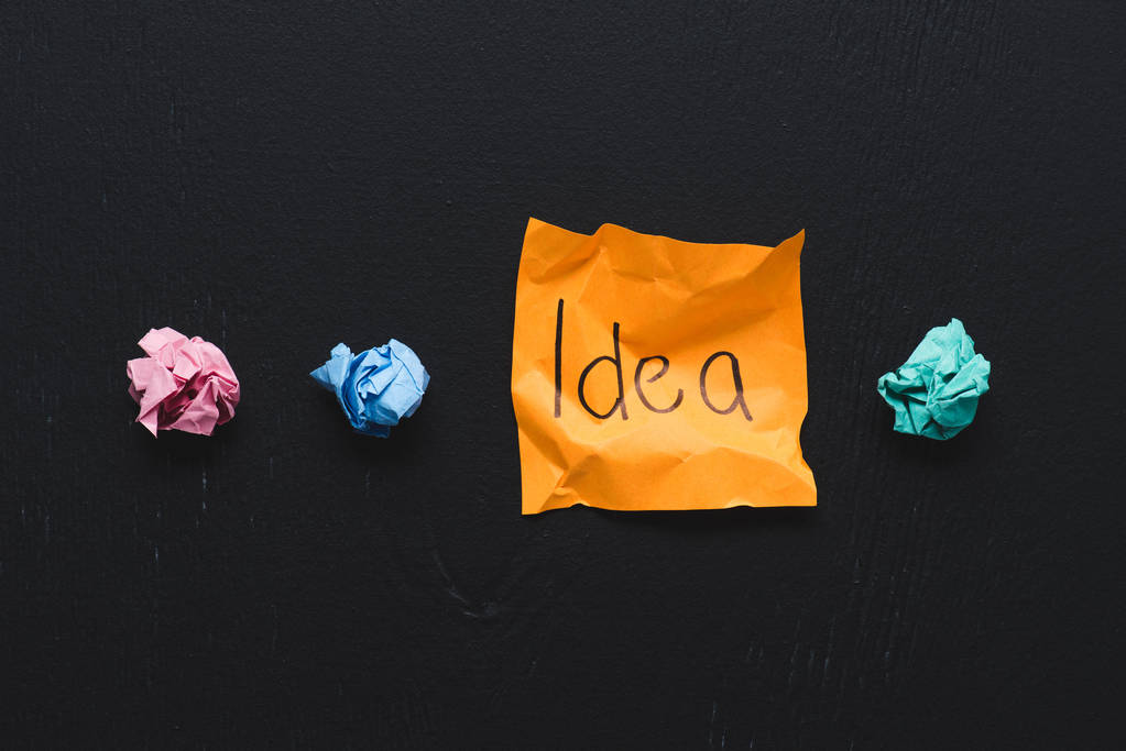 vista superior de la palabra 'idea' escrita en nota adhesiva con bolas de papel arrugadas de colores sobre fondo negro, concepto de ideas
 - Foto, Imagen