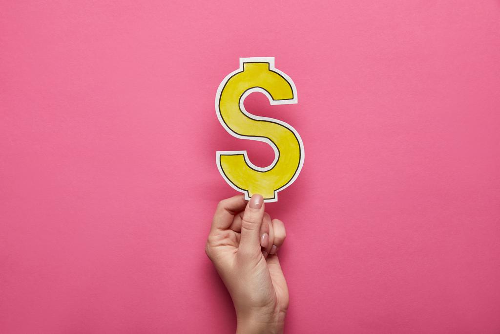 top view of hand holding yellow dollar sign on pink background - Photo, Image
