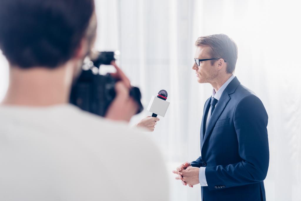 вибірковий фокус красивого бізнесмена в окулярах дає відео-інтерв'ю журналісту в офісі
 - Фото, зображення
