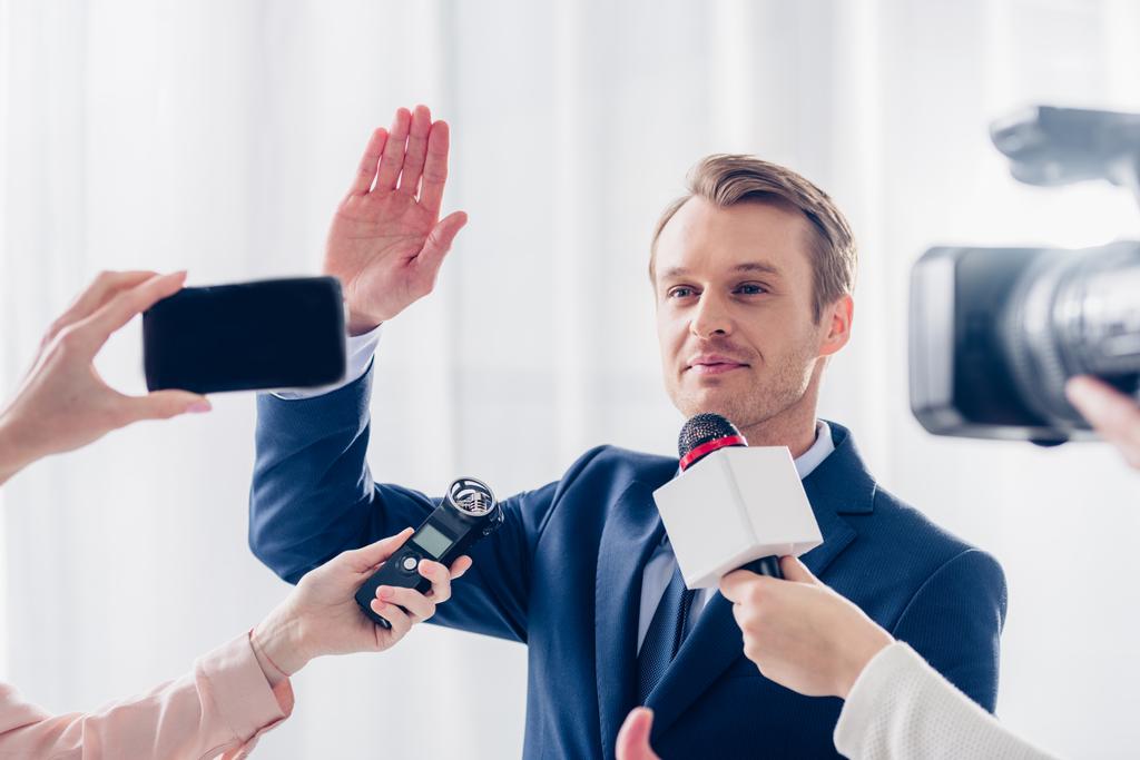 handsome businessman giving interview to journalists in office and waving hand - Photo, Image