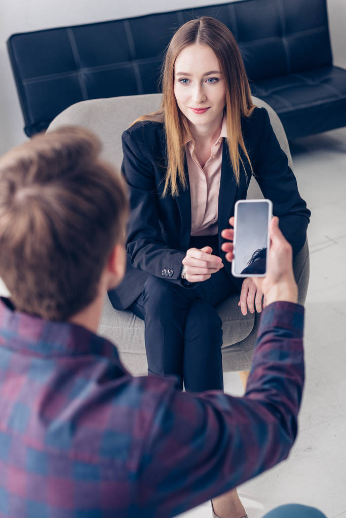 hoge hoekmening van journalist opname interview met zakenvrouw op smartphone in kantoor - Foto, afbeelding