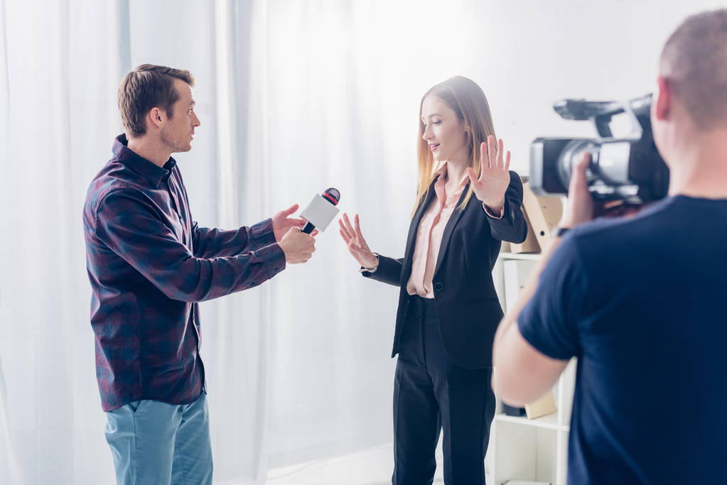 オフィスでカメラマンにスーツのジャーナリストおよび表示停止にインタビューを与えることを拒否することの美しい女性実業家を歌う - 写真・画像