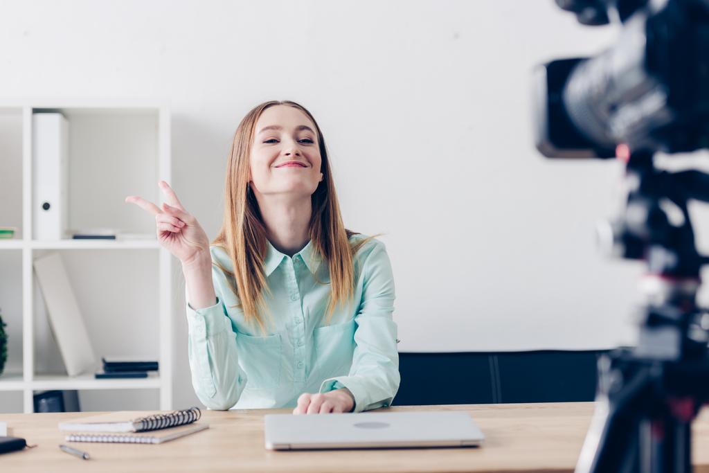 vonzó női videóinak blogger felvétel vlog, és bemutatja a két ujjal irodában mosolyogva - Fotó, kép