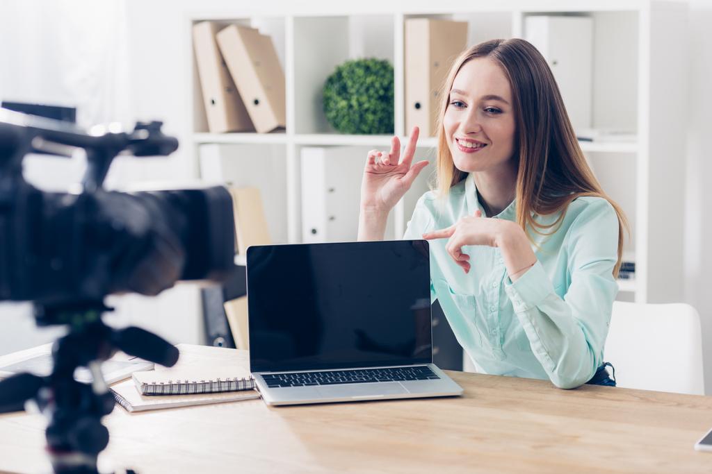 lachende aantrekkelijke vrouwelijke video blogger opname vlog in kantoor, laptop met leeg scherm op tafelblad - Foto, afbeelding