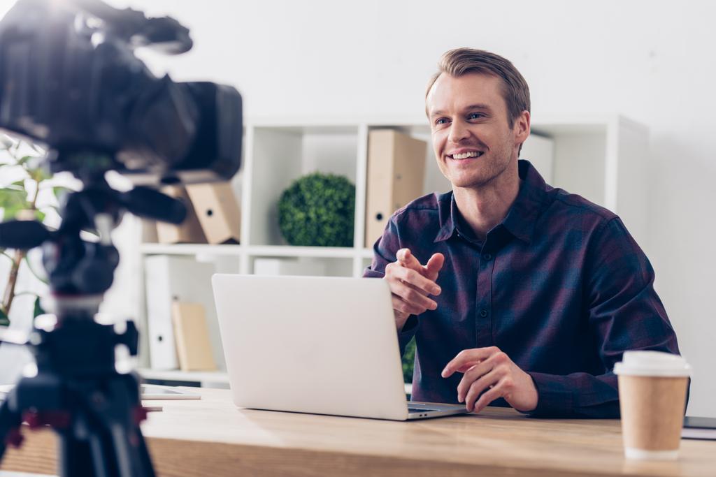 lächelnd gut aussehender männlicher Videoblogger im violetten Hemd, der Videoblog im Büro aufzeichnet - Foto, Bild