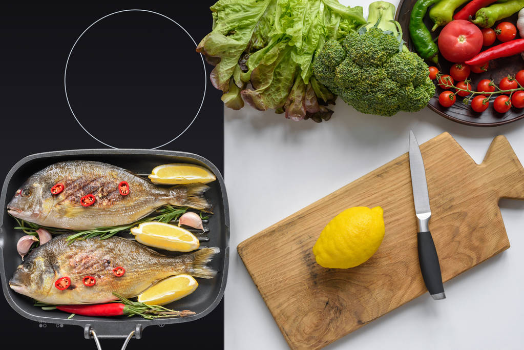 top view of delicious fish on grill and fresh vegetables with cutting board and knife - Photo, Image