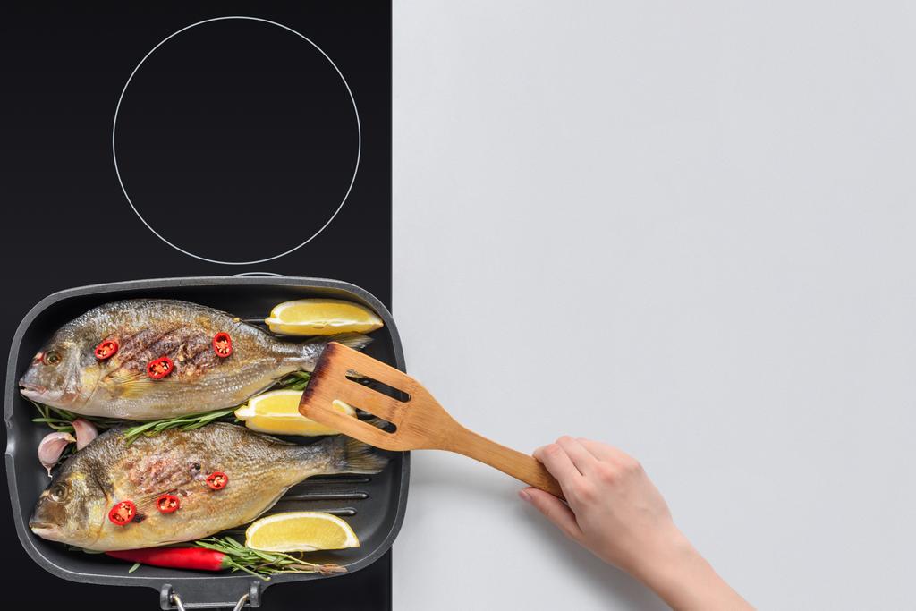 abgeschnittene Aufnahme einer Person mit hölzernem Utensil, die köstlichen gebratenen Fisch kocht - Foto, Bild
