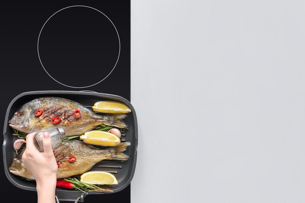 przycięte sklep osoby dodanie soli podczas gotowania ryb z rozmarynem i cytryny na grill  - Zdjęcie, obraz