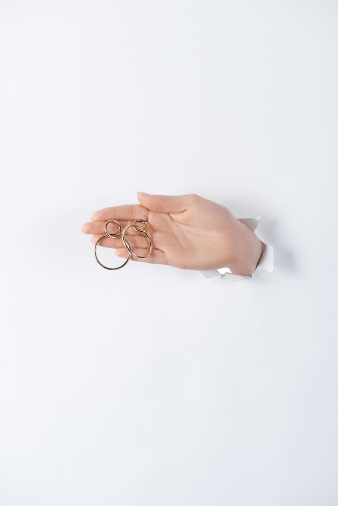 imagen recortada de la mujer cogida de la mano con hermosos pendientes redondos de oro a través de papel blanco
 - Foto, Imagen