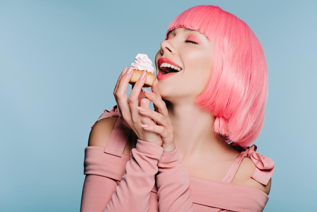 opgewekt meisje in roze pruik houden van zoete cupcake geïsoleerd op blauw - Foto, afbeelding