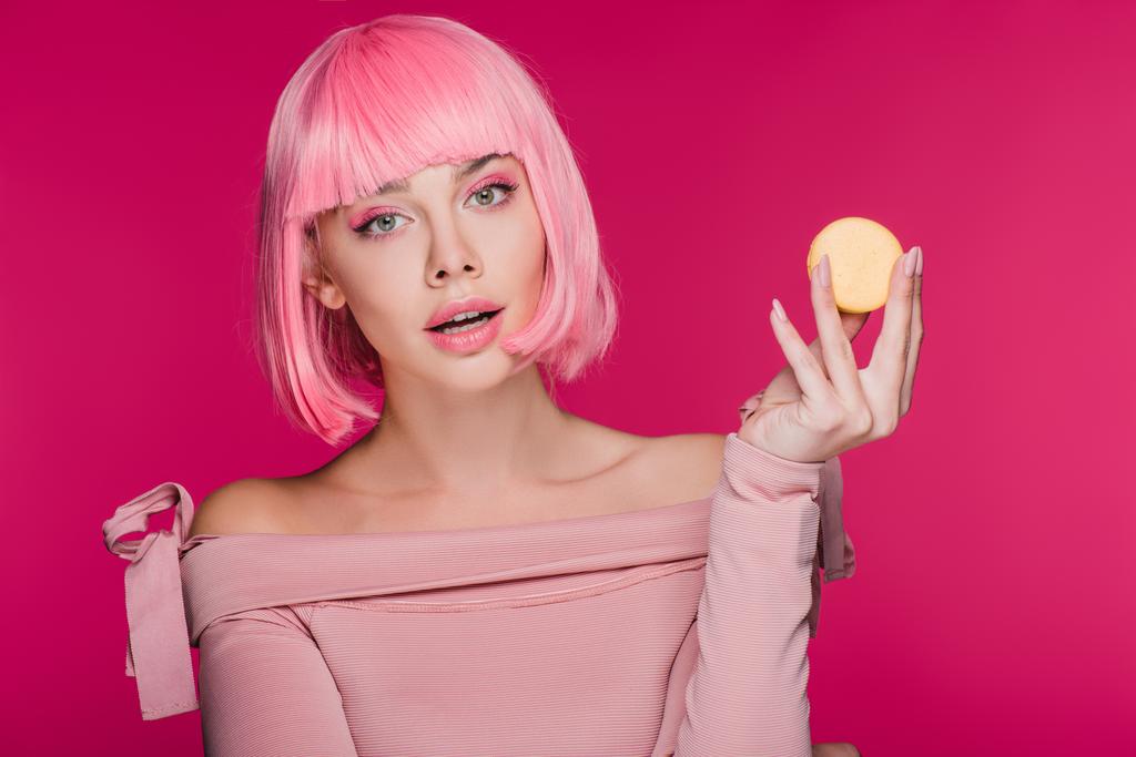 attractive fashionable girl in pink wig posing with yellow macaron isolated on pink - Photo, Image