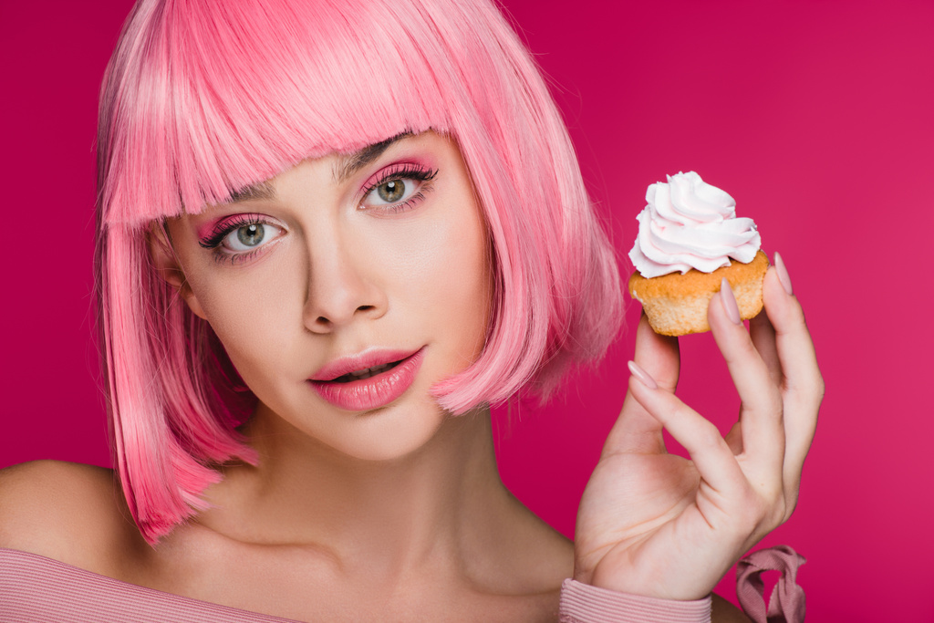 menina bonita em peruca rosa segurando delicioso cupcake isolado em rosa
 - Foto, Imagem