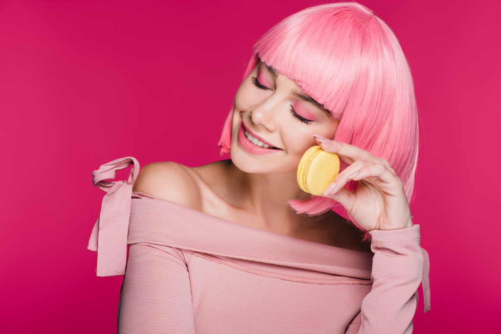 donna sognante sorridente in parrucca rosa in posa con macaron isolato su rosa
 - Foto, immagini