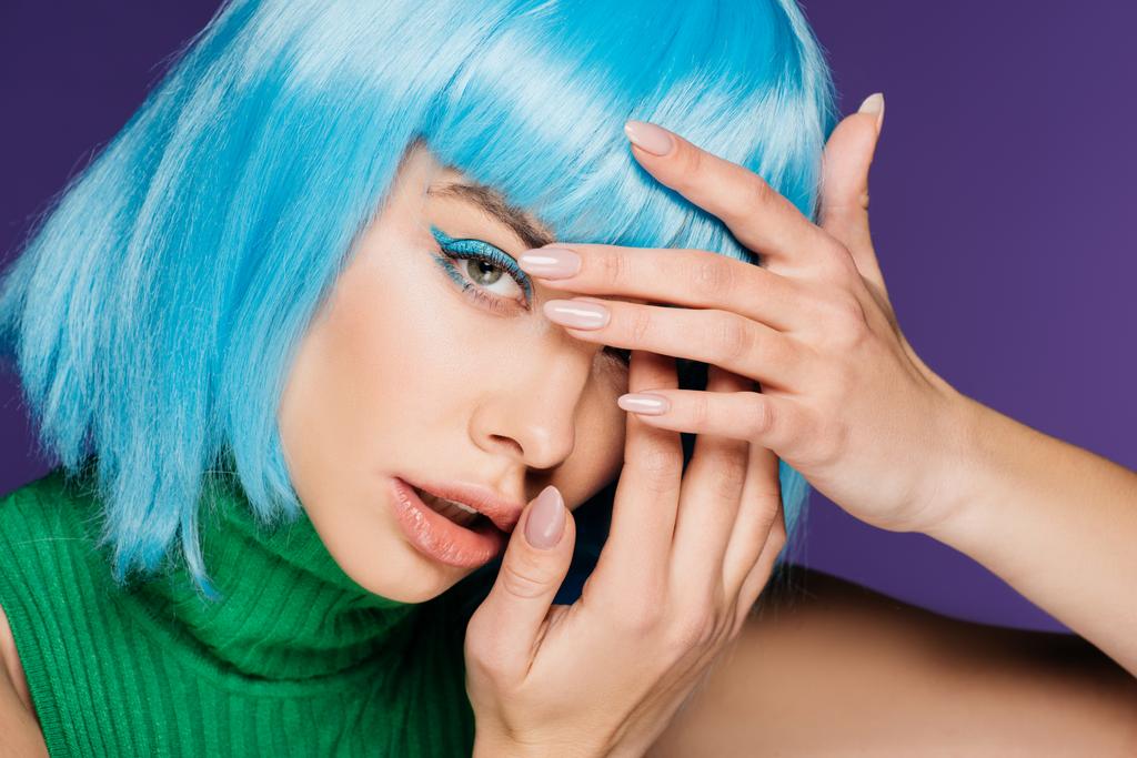 красивая девушка с голубым макияжем и париком показывая ногти с маникюром, изолированные на фиолетовый
 - Фото, изображение