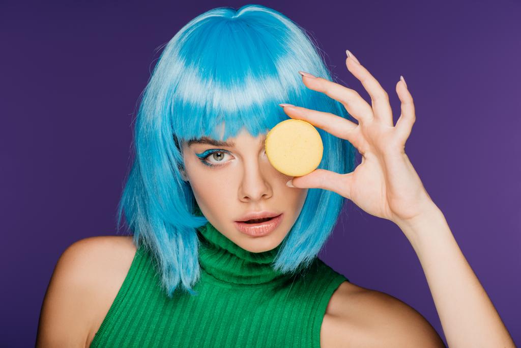 attractive sensual girl in blue wig posing with macaron isolated on purple - Photo, Image