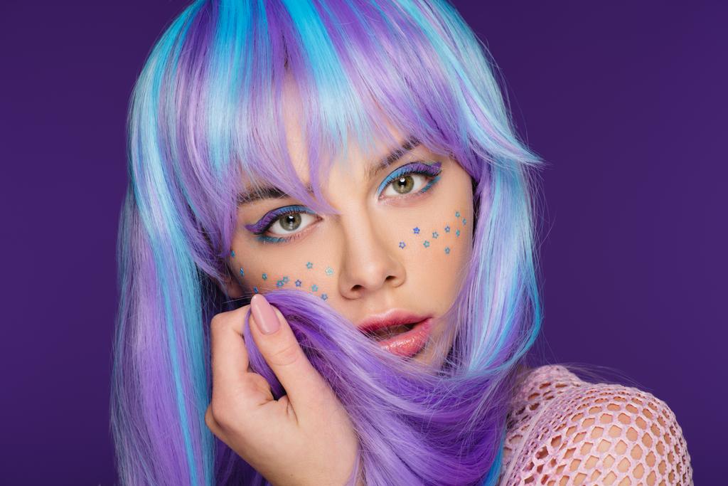trendy jonge vrouw poseren in violet pruik met sterren op gezicht, geïsoleerd op paars - Foto, afbeelding