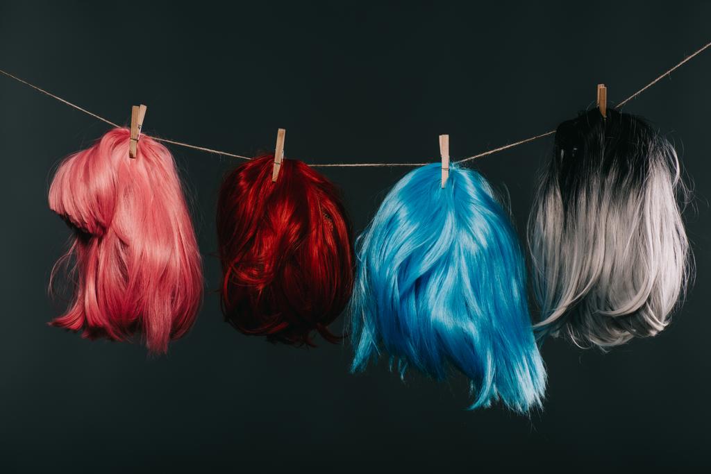 quatre perruques colorées accrochées à une corde isolée sur du noir
 - Photo, image