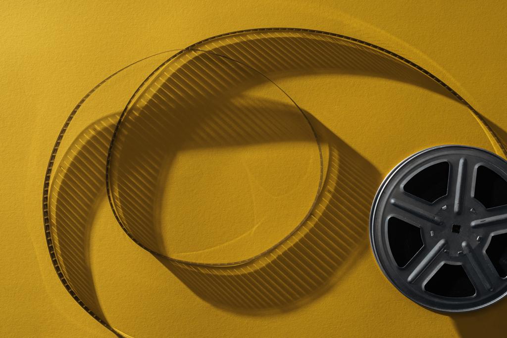 top view of movie reel with twisted cinema tape on yellow background - Photo, Image